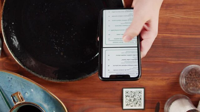 Woman using online menu in cafe top view, scanning qr code with smartphone in restaurant . Modern technology, ordering meal in application. Contactless touch-free payment in app.