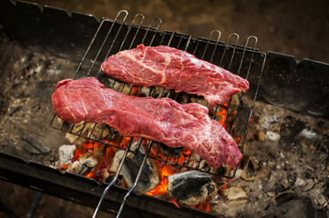 Two raw marbled beef steaks are grilled in the dark in the evening. Defocus