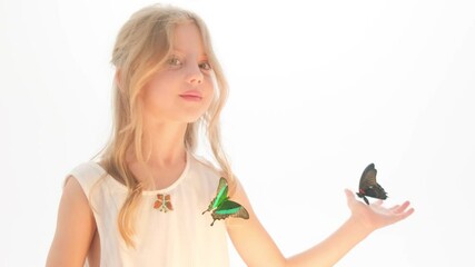 Beautiful little girl in a dress in the studio on a white background plays with real big butterflies.