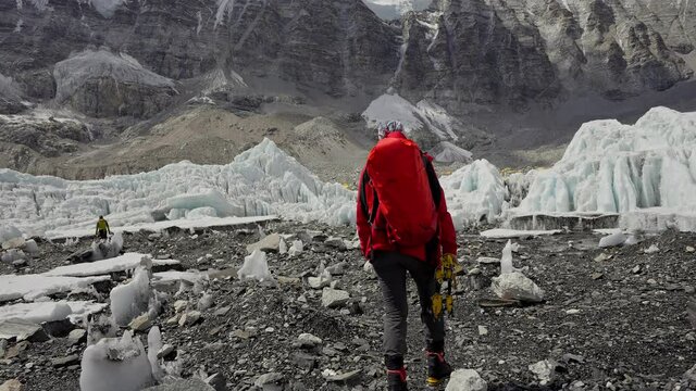 Alpinist with red backpack walk on rocky path along glacial to Everest Base Camp
