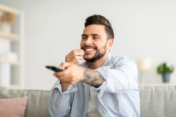 Happy relaxed guy watching Tv and eating popcorn, switching channels with remote controller, resting on couch