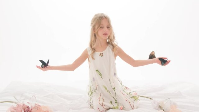 Beautiful little girl in a dress in the studio on a white background plays with real big butterflies.