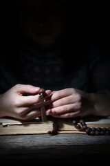 Young beautiful girl praying to God with wooden rosary. Selective focus on cross and hands.