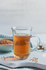 Glass cup of Egyptian fenugreek yellow tea, Helba or Methi Dana drink and fenugreek seeds on light blue background