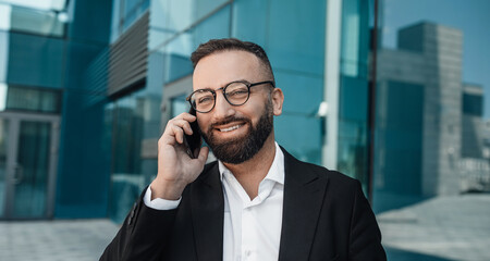 Business call. Confident bearded businessman chatting on cellphone standing outdoor in city