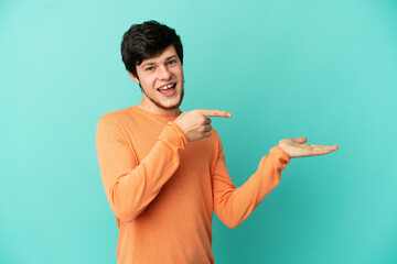 Young Russian man isolated on blue background holding copyspace imaginary on the palm to insert an...