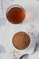 Glass of Egyptian fenugreek yellow tea, Helba or Methi Dana drink and fenugreek seeds on white wooden background