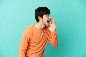 Young Russian man isolated on blue background shouting with mouth wide open to the side
