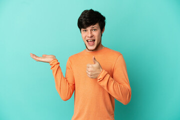 Young Russian man isolated on blue background holding copyspace imaginary on the palm to insert an...