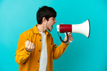 Young Russian man isolated on blue background shouting through a megaphone to announce something in lateral position