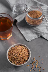 Bowl of fenugreek seeds and Egyptian fenugreek yellow tea or Methi Dana drink on grey background