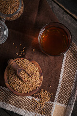 Glass of Egyptian fenugreek yellow tea, Helba or Methi Dana drink and fenugreek seeds on dark wooden background