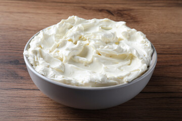 Bowl of tasty cream cheese on wooden table
