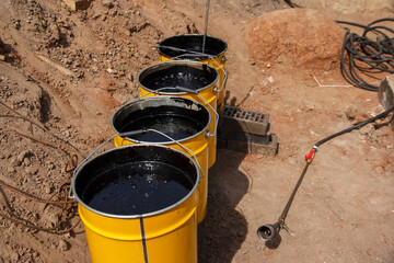 Bitumen mastic in buckets. Protective bitumen mastic for concrete pavement. Material for waterproofing the foundation.