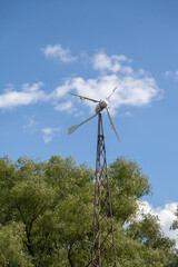 Household wind turbine over green trees
