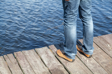 Legs in jeans stand on wooden bridge over river