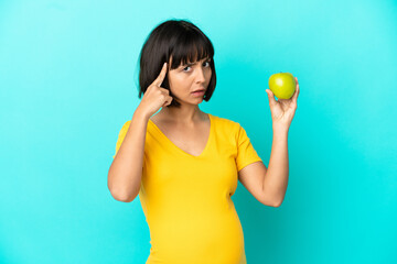 Pregnant woman holding an apple isolated on blue background thinking an idea