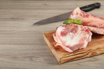 Cutting board with raw chopped meaty bones and basil on wooden table. Space for text