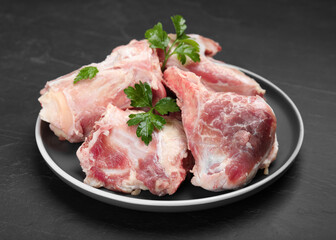 Plate with raw chopped meaty bones and parsley on black table