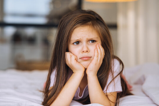 Cute little girl with a sad face lying on the bed