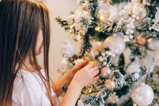 Adorable little girl decorating a Christmas tree with baubles at home