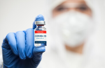 Medical NHS worker holding COVID-19 SARS-CoV-2 vaccine glass ampoule vial,wearing personal protective gear,white clean suit,blue gloves,Coronavirus cure,virus disease prevention and protection concept