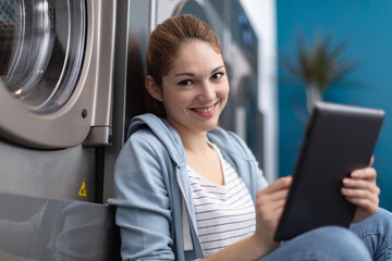 portrait of young woman holding digital tablet in laundromat
