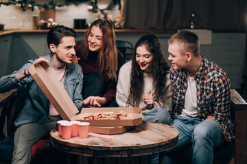 Young people socialize at a non-alcoholic pizza party in the living room. A man with a disability has fun with friends