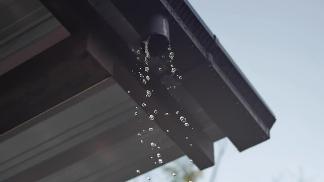 Slow motion of water being drained from aluminum roof through metallic gutter