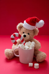 Santa teddy and Christmas hot beverage, mug with marshmallows and candy cane on red color background