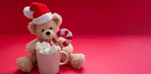 Santa teddy and Christmas hot beverage, mug with marshmallows and candy cane on red color background