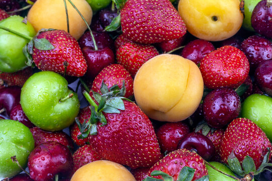Fresh Summer fruit background. Ripe strawberry, apricot, cherry, green plum close up image.