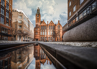 Fototapeta premium Brindley Place red brick church building reflected in water. West Midlands landmark buildings redevelopment in historic city centre reflection in stream. Birds and clouds in sky.