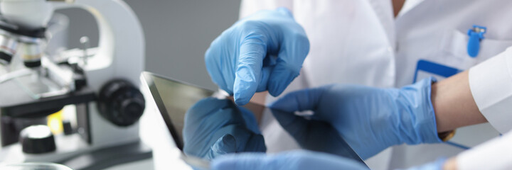 Scientists in sterile gloves hold tablet in laboratory closeup