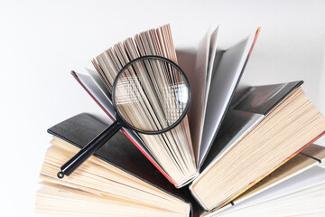 Magnifying glass over open paper book with pages. Concept of academic research, search and studying.