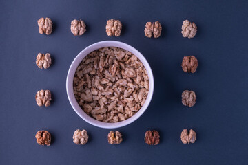 Chopped walnuts in a deep bowl, beautiful whole walnut kernels lie around a dark background. The...