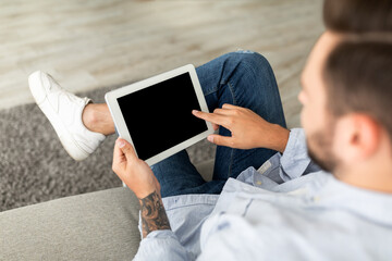 Young man using digital tablet with blank black screen, browsing website or showing new app,...