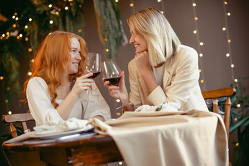 lesbian couple having dinner in a restaurant. Girls drink wine and talk - obrazy, fototapety, plakaty