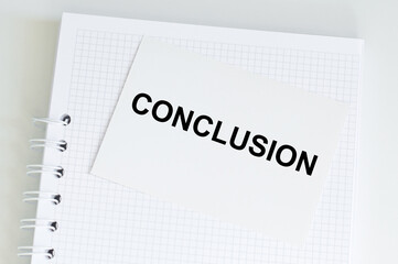 A white card with the text CONCLUSION on notepad on table