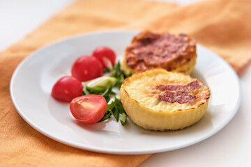 Two portioned round-shaped baked omelette, halves of cherry tomatoes, chopped green onions on white...