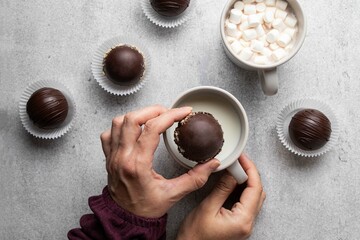 Woman's hand dropping chocolate cocoa bomb into hot cup of milk. Holiday winter drink. Handmade...
