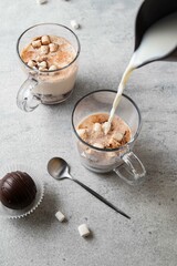 Hot milk pouring into a mug with cocoa chocolate ball bomb with marshmallow. Bomb melts in hot milk. Holiday winter drink. Handmade Christmas present. Comfort food. Selective focus.