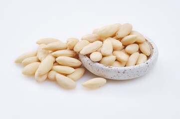 Pile of peeled or blanched almonds. White bowl of peeled whole almonds on white background. Shallow...