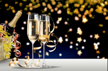 Glasses and bottle of champagne with serpentine streamers against lights on background.
