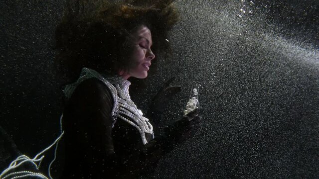mysterious woman is floating under water and playing with pearls, underwater queen or witch