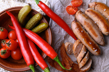 Top view of grilled sausages, chili peppers, pickled cucumbers and tomatoes