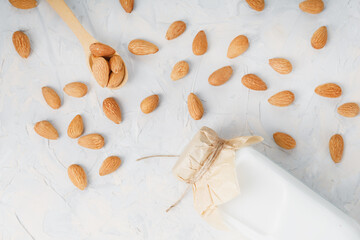 Milk from organic almonds in a transparent bottle with a scattering of seeds and a wooden spoon on a light background