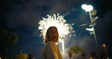 Young happy and excited woman watch fireworks on holiday festival day or celebration, look back at camera and smile, authentic laugh and emotions. Amusing festivities in outdoor location