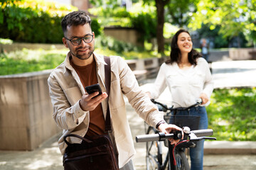 Happy young couple outdoors. Loving couple with bicycle in the park, Handsome man using the phone.