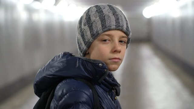 Portrait of alone confident boy in hat and jacket in underground covered walkway in city at winter